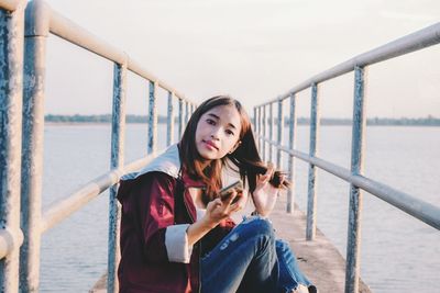 Portrait of young woman using phone while standing on railing