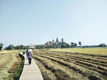 Rear view of woman walking on field against clear sky