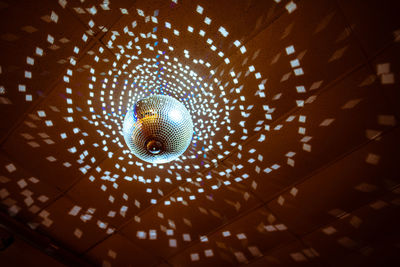 Low angle view of illuminated disco ball hanging from ceiling in nightclub