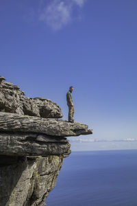 Statue on rock by sea against clear blue sky