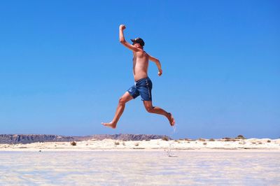 Full length of shirtless man jumping at beach against clear sky