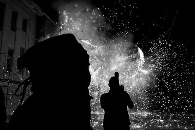 Silhouette man playing fireworks by building