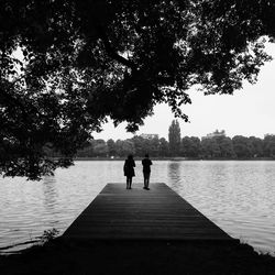 Rear view of people standing on pier over lake