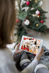 Girl video conferencing while holding digital tablet by christmas tree