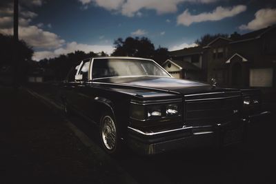 Vintage car on street by houses against sky