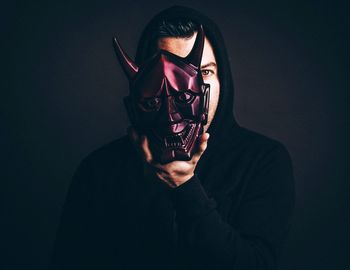 Portrait of young man wearing mask against black background
