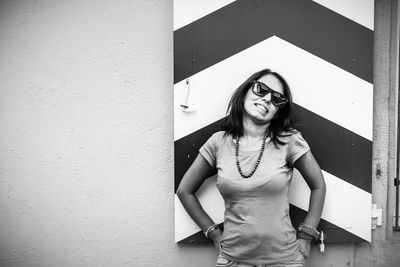 Portrait of smiling woman wearing sunglasses while standing against wall