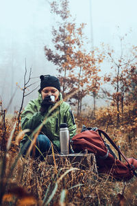 Woman with backpack having break during autumn trip drinking a hot drink from thermos flask