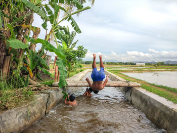 Man with children swimming in canal against sky