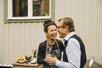 Senior man and woman laughing while holding drink at back yard during party