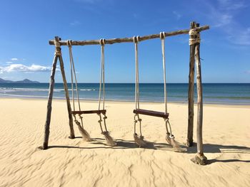 Wooden swing on beach against sky