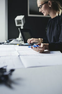 Female engineer holding pen while using calculator on desk at home office