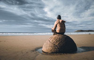 A man sitting on the rock at moeraki boulders new zealand.