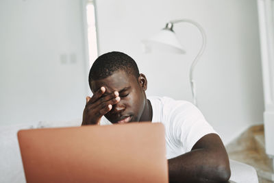 Tired man rubbing eyes by laptop at home