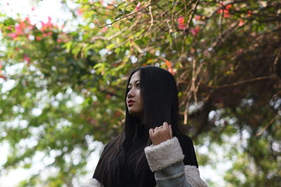 Young woman looking away against trees