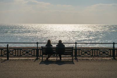 Rear view of silhouette friends sitting on railing against sea