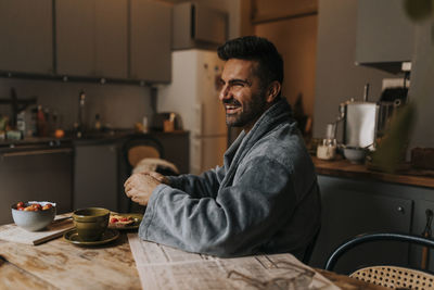 Happy man wearing bathrobe while having breakfast at home