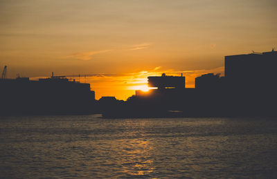 Silhouette buildings by sea against sky during sunset