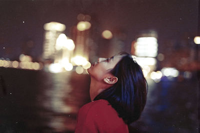 Side view of thoughtful woman standing against illuminated city at night