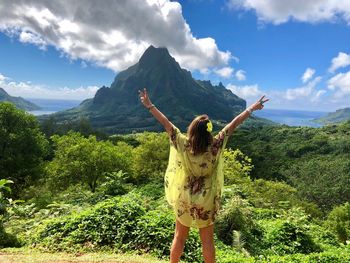 Rear view of woman with arms raised standing against mountain