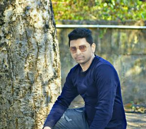 Young man wearing sunglasses standing against trees