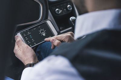 Man in car adjusting smart home device via smartphone