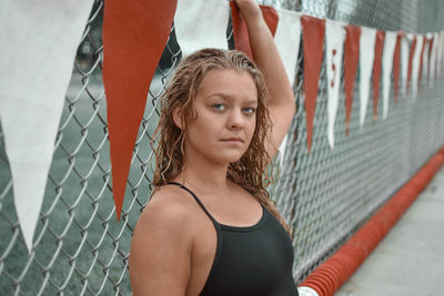 Portrait of young woman in swimwear by chainlink fence