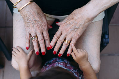 Hand of baby girl pointing on hand of senior woman with rings and red painted nails