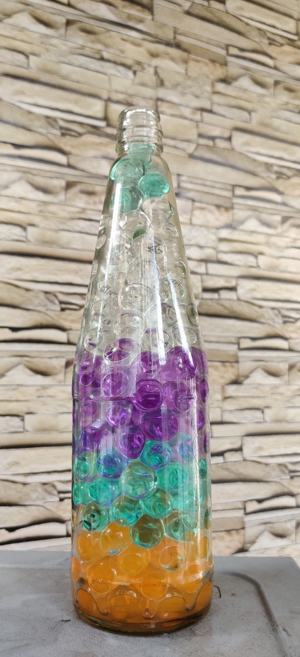 CLOSE-UP OF MULTI COLORED GLASS WITH BOTTLE ON TABLE
