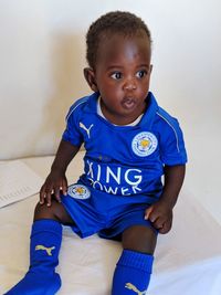 Portrait of cute boy sitting against blue wall