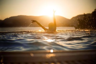 Silhouette man swimming in sea against sunset sky