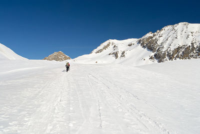 Person walking on snowcapped mountain against clear sky