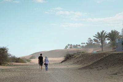 Rear view of people walking on sand dune