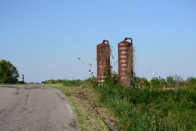 Damaged road amidst plants against clear blue sky