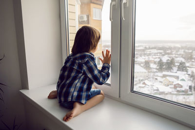 Child boy sits on a window sill in winter on a high floor