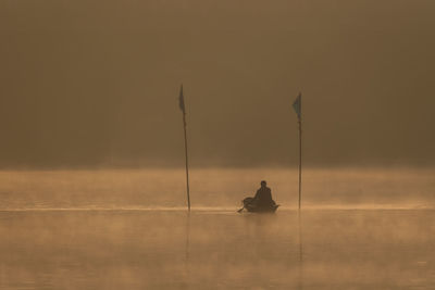 Silhouette of man sitting in boat on lake during sunset