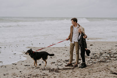 Young attractive couple having fun at he beach with a dog