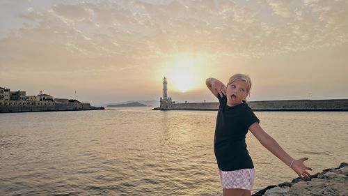 Rear view of girl standing by sea against sky during sunset