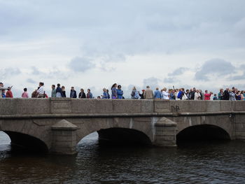 People on bridge over river against sky