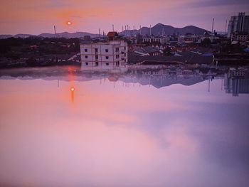 Scenic view of lake by buildings against sky at sunset