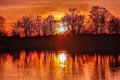 Silhouette trees by lake against sky during sunset