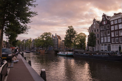 Canal in city against cloudy sky during sunset