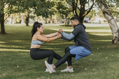 Couple holding hands while doing crouching exercise together at backyard