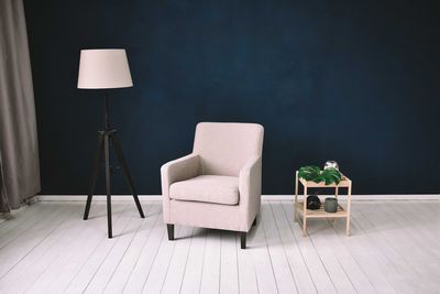 Empty chair by floor lamp against wall at home