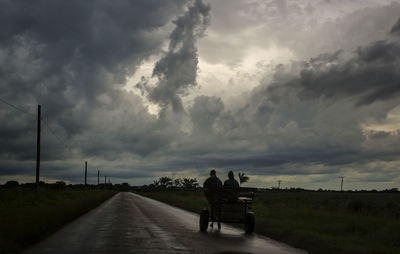 Rear view of people on road against cloudy sky