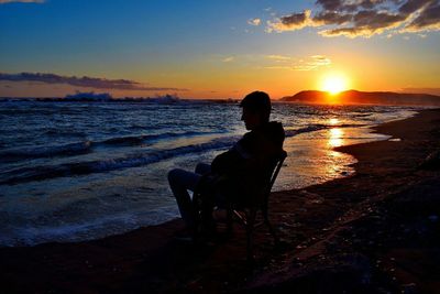 Rear view of silhouette woman sitting on beach at sunset