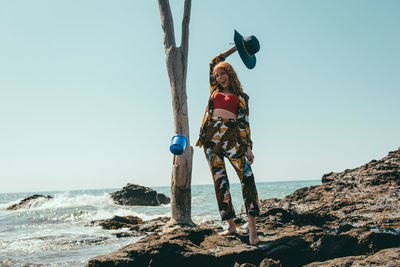 Portrait of woman standing on rock by sea against clear sky