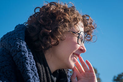 Close-up portrait of young woman looking away against blue sky