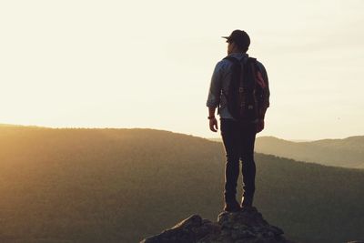 Rear view of man standing on rock against sky during sunset