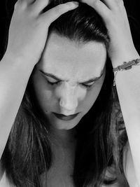 Close-up of young woman with headache against black background